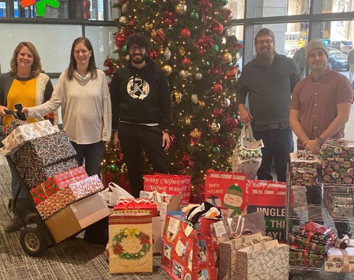 Team members standing around a tree with gifts collected during the holidays