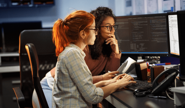 Two female software engineers coding on a computer while at work.