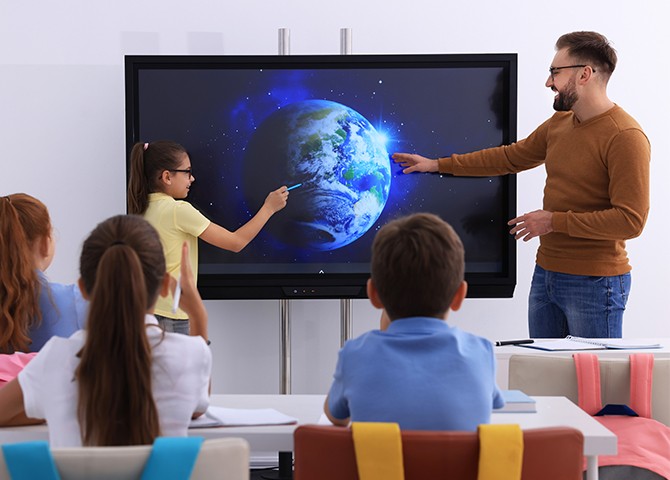 Modern teacher using a smart board with students in a classroom, demonstrating innovative teaching methods and technology integration.